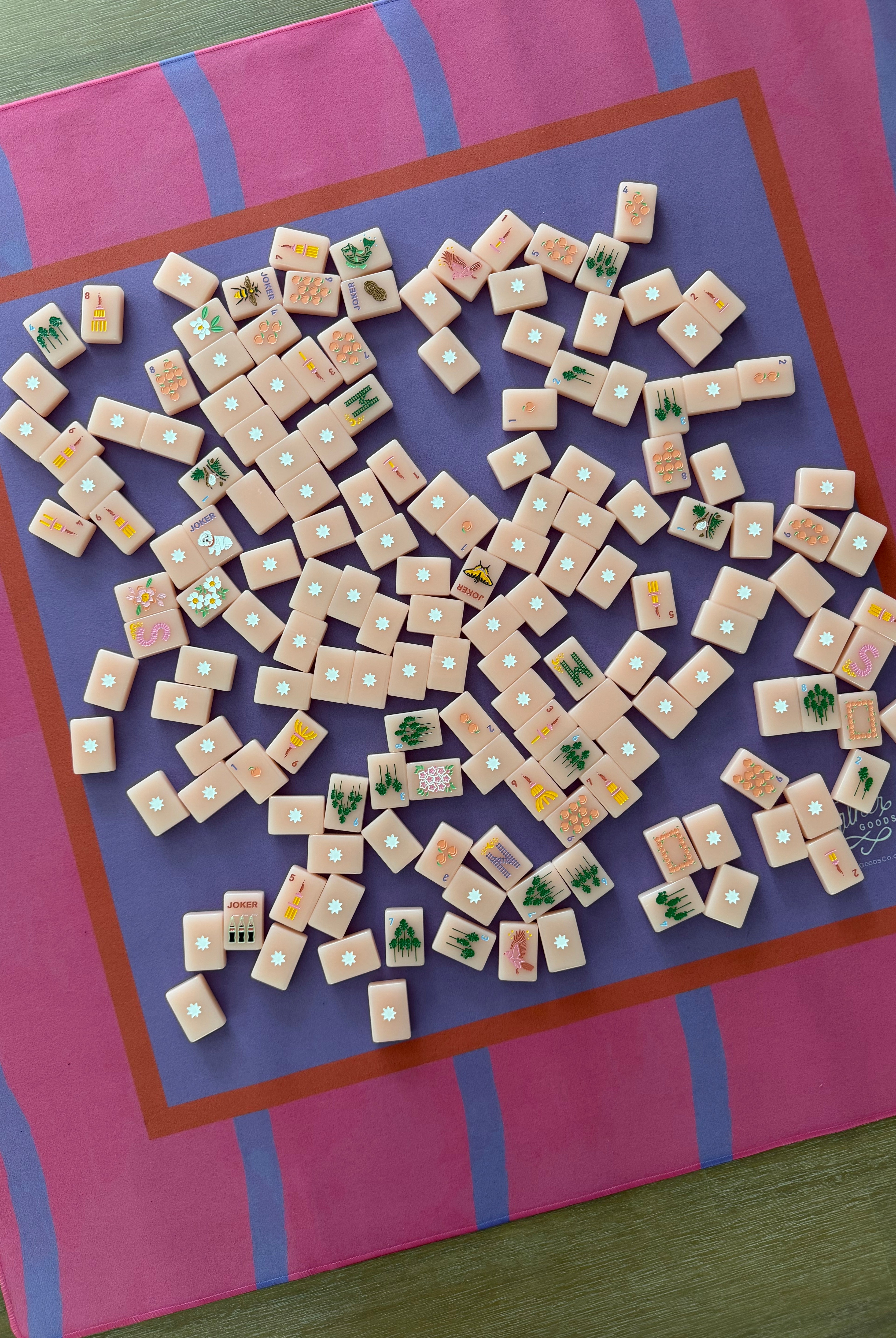 A top-down view of Mahjong tiles scattered on a Maximalist hot pink and lavender wavy stripe mahjong mat