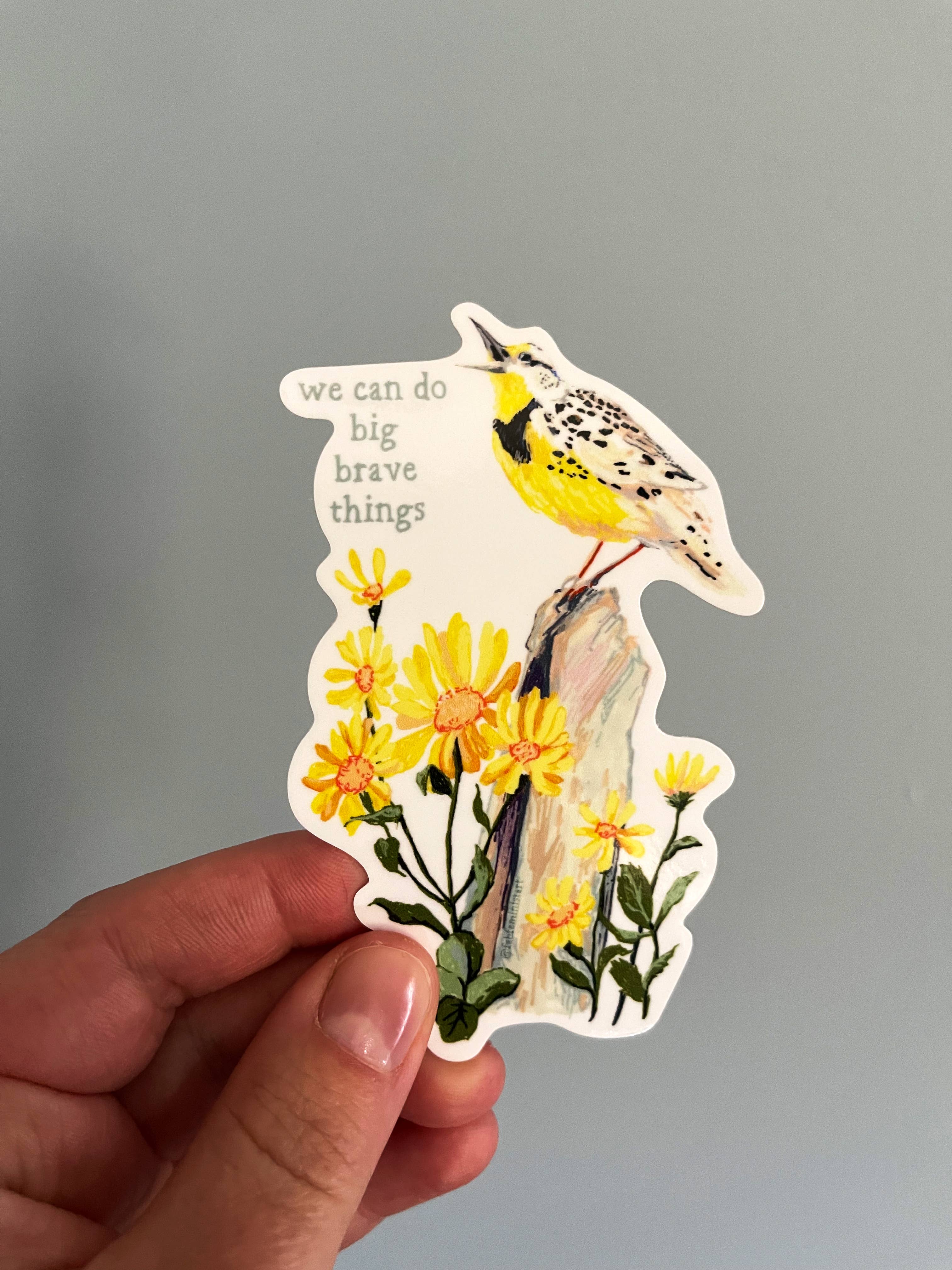 A sticker with an illustration of a bird perched on a flower, with the phrase 'we can do big brave things' written above.
