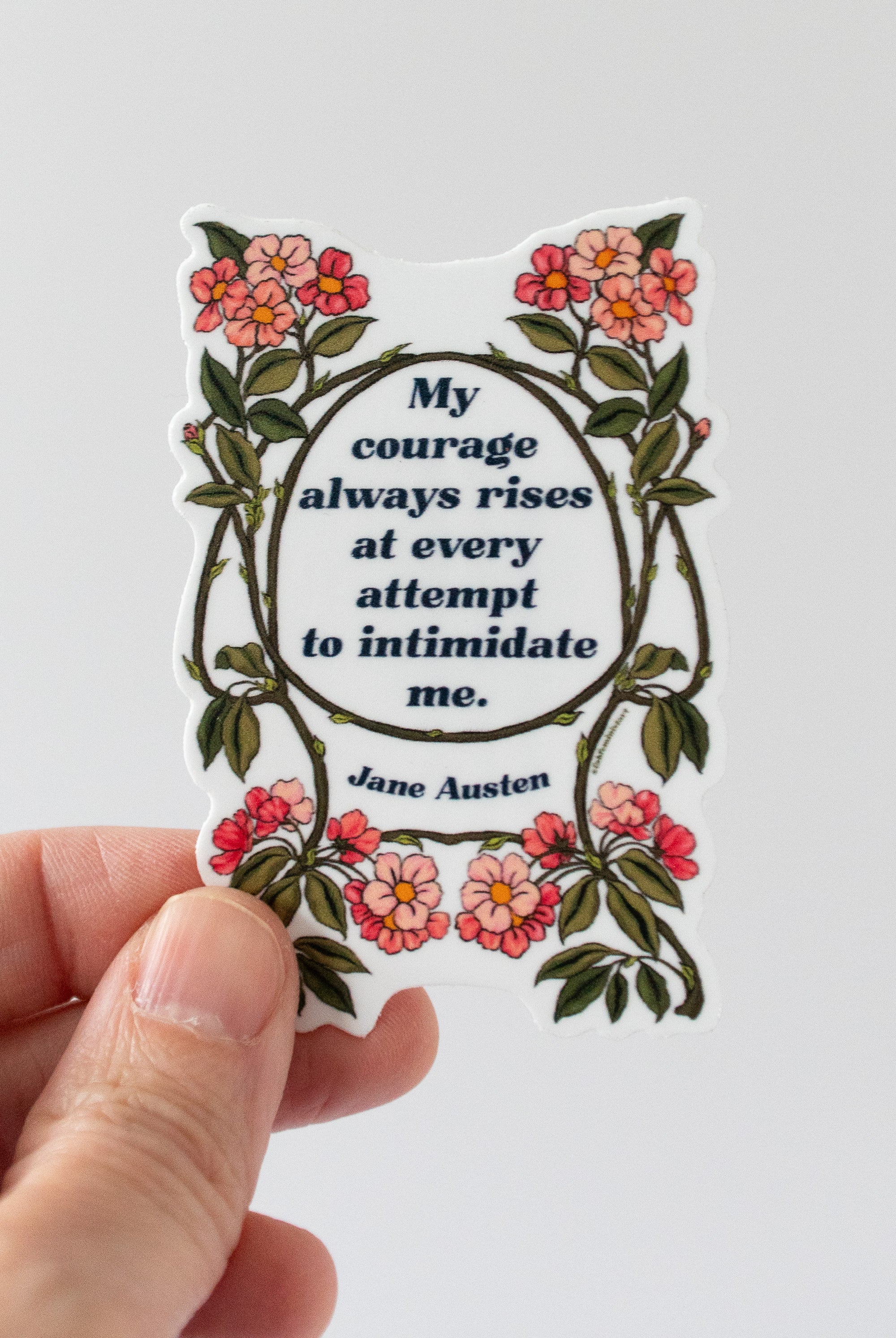 A sticker with a quote by Jane Austen, surrounded by floral designs in red and green colors.