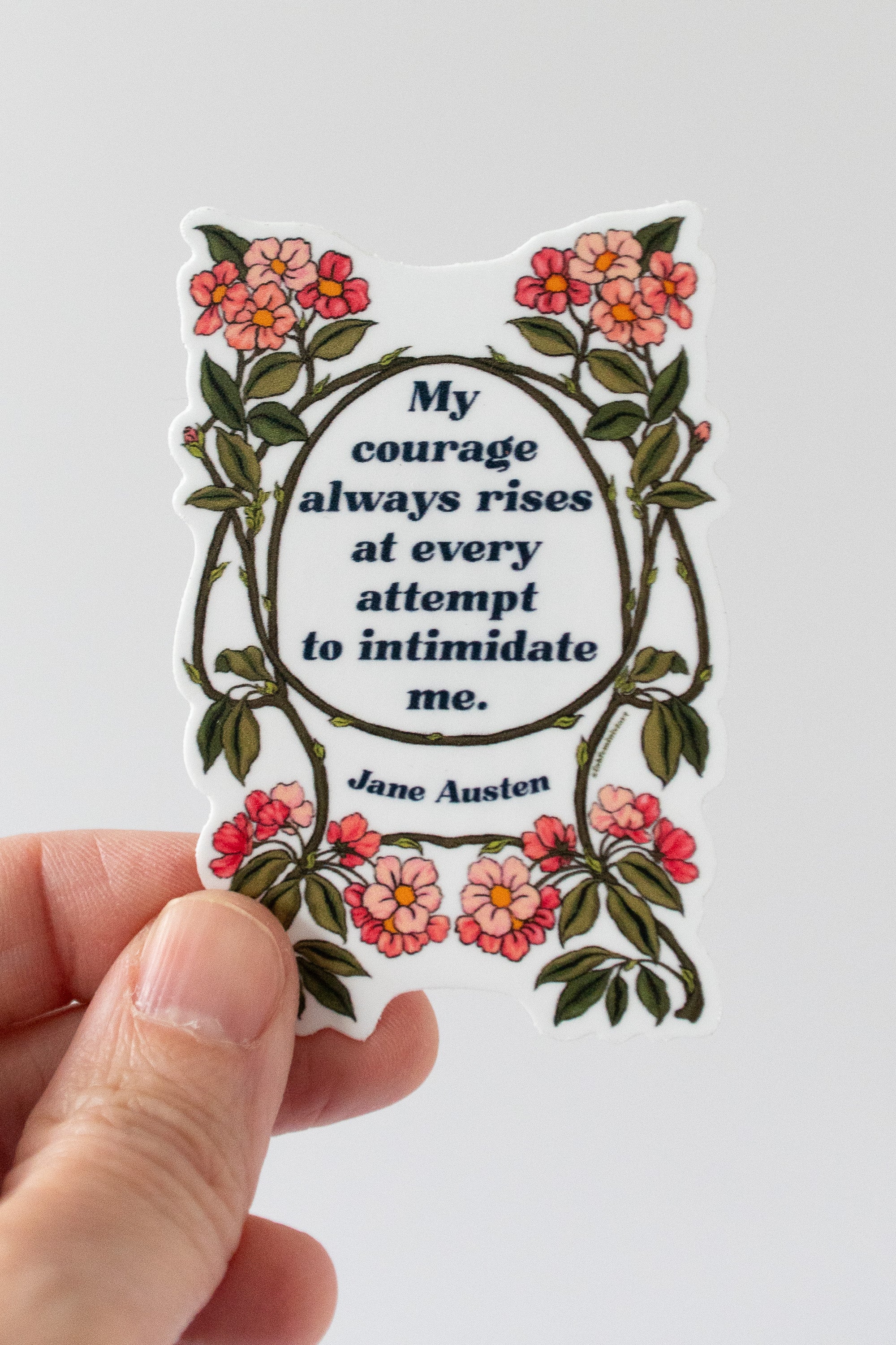 A sticker with a quote by Jane Austen, surrounded by floral designs in red and green colors.