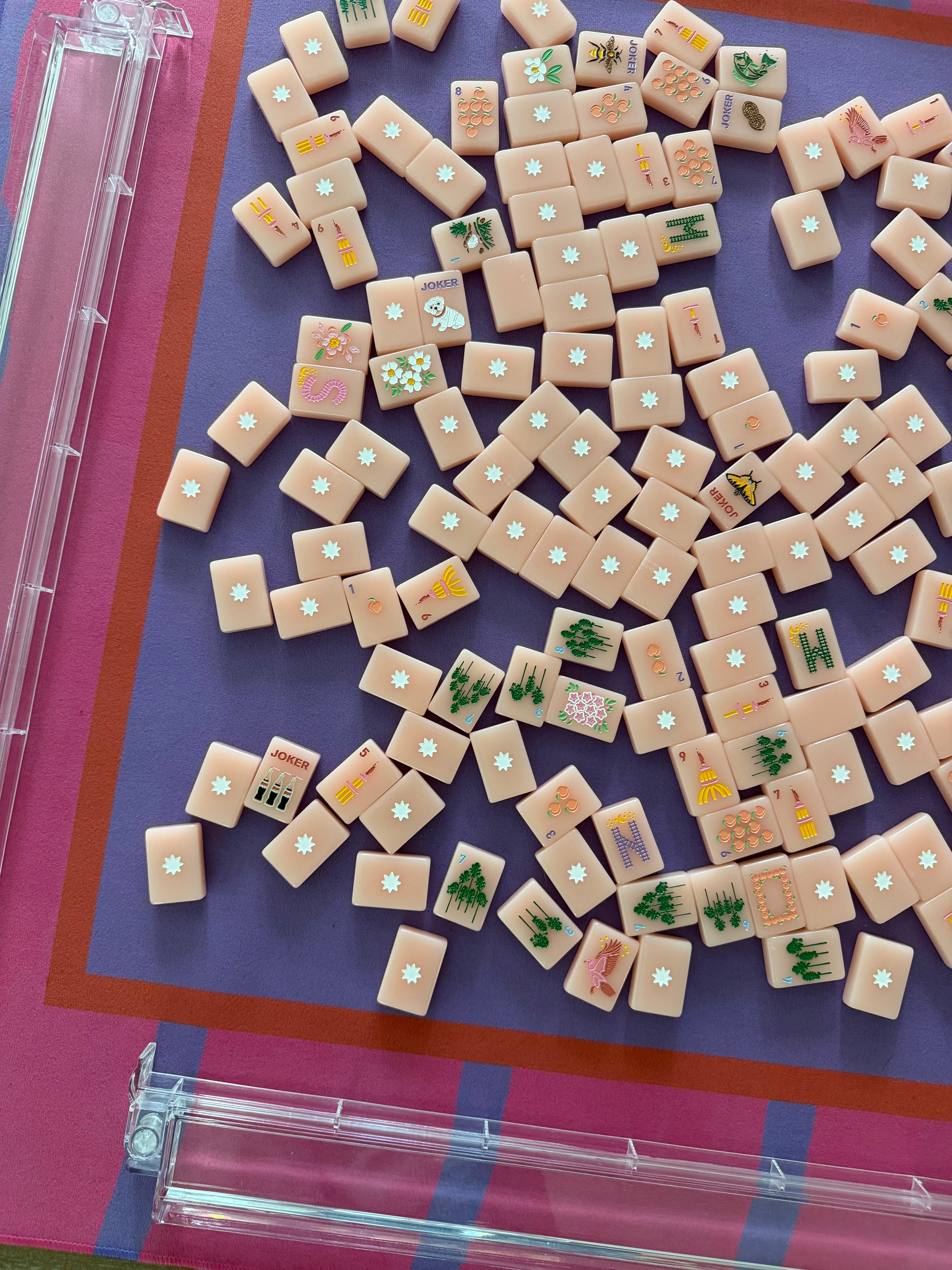 Maximalist hot pink and lavender wavy stripe mahjong mat with peach colored mahjong tiles. Close up of a mahjong table setup