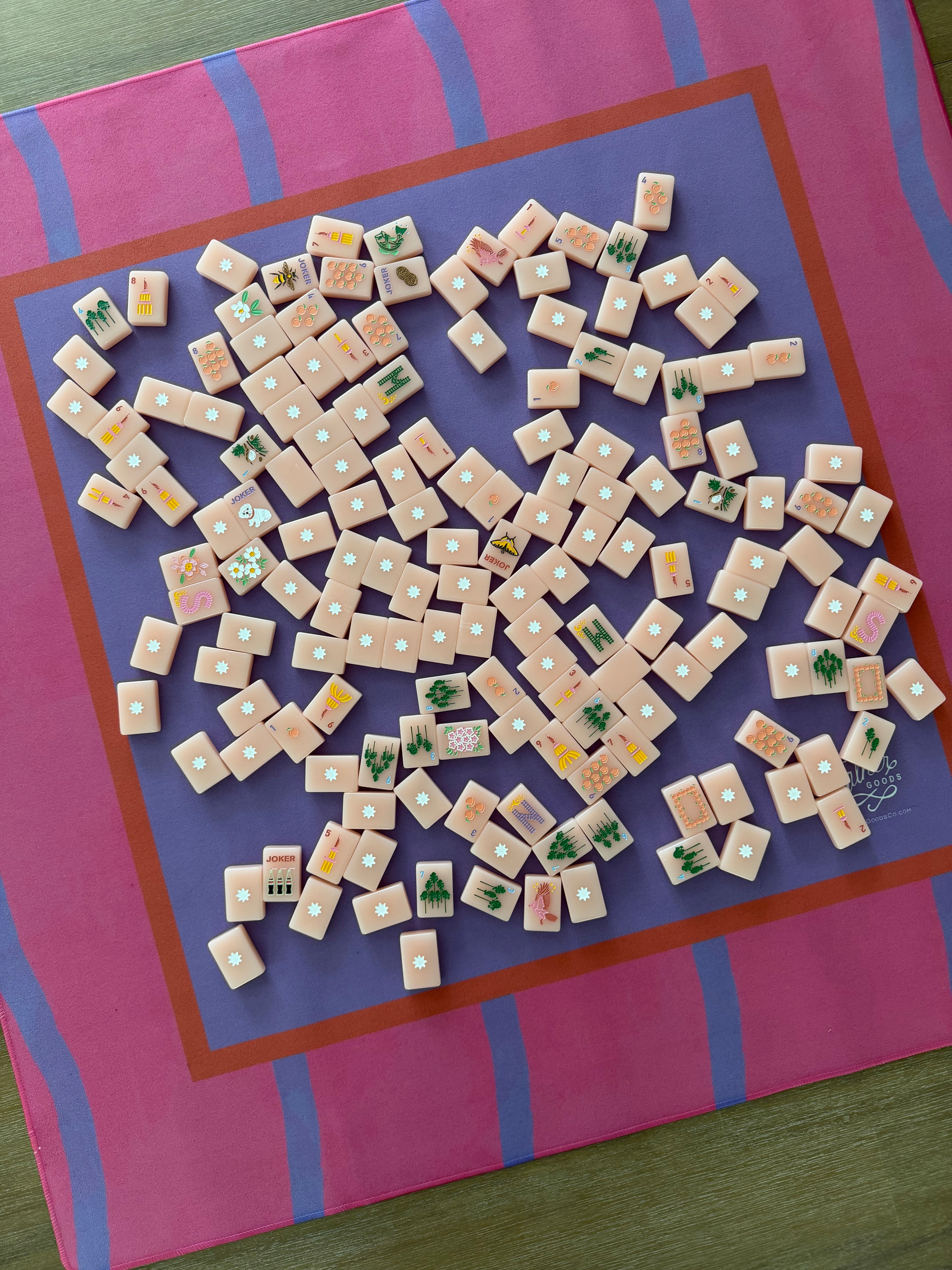 A top-down view of Mahjong tiles scattered on a Maximalist hot pink and lavender wavy stripe mahjong mat