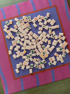 A top-down view of Mahjong tiles scattered on a Maximalist hot pink and lavender wavy stripe mahjong mat
